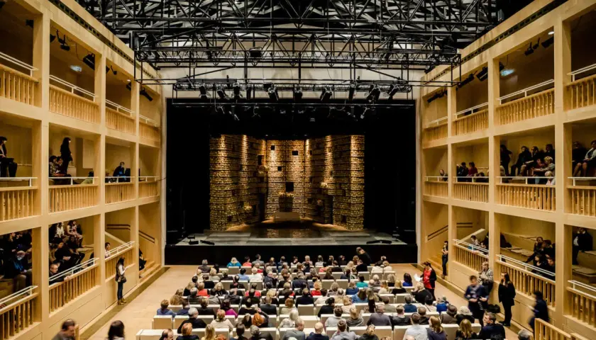 Widownia i scena w nowoczesnym teatrze królewskim w starej oranżerii. Drewniane galerie otaczają salę, a widownia zajmuje miejsca przed sceną.