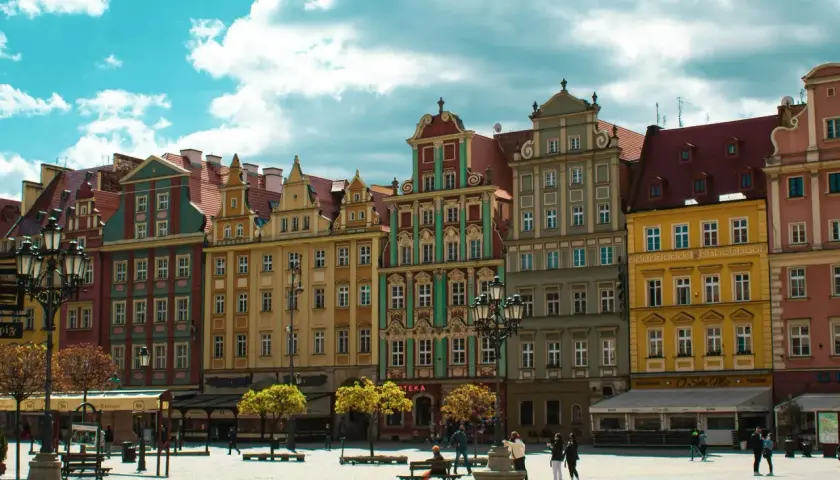 Kolorowe kamienice na starym rynku we Wrocławiu, z błękitnym niebem i białymi chmurami w tle.