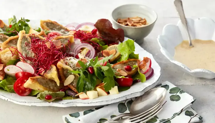 Herzhafter Maultaschen Salat mit knackigem Gemüse, roten Zwiebeln, Granatapfelkernen und Mandelsplittern. Dazu eine cremige Sauce.