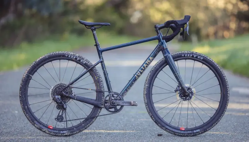 A dark blue Juliana gravel bike with gold lettering sits on a paved path, ready for adventure.
