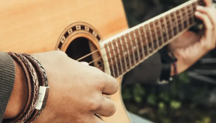 Dłoń grająca na gitarze, tworząca akord e moll. Na nadgarstku widać bransoletkę ze skóry.