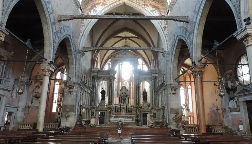 Intérieur de l'église Santo Stefano à Venise, avec ses bancs en bois, ses voûtes ornées et son autel baigné de lumière.
