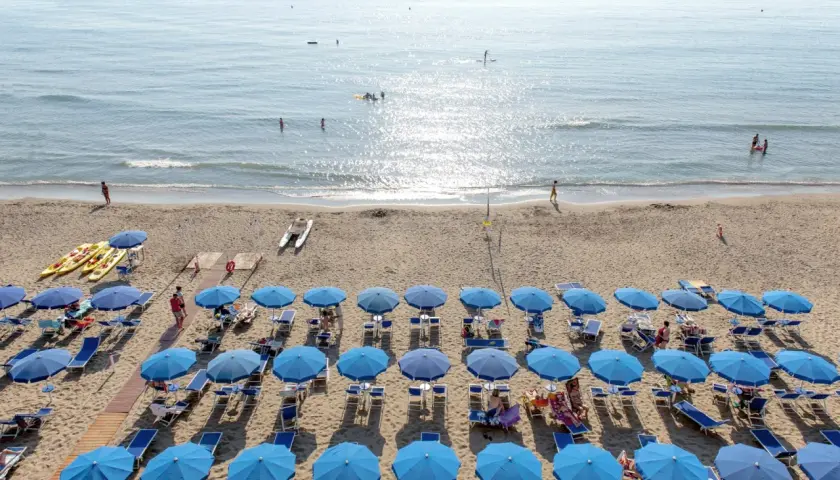 Plage de San Vincenzo en Toscane, avec des rangées de parasols bleus, des kayaks et des gens profitant de la mer.