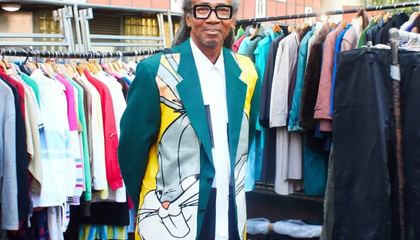 Man in a Bugs Bunny jacket stands by racks of colorful clothes, a testament to creative clothes upcycling.