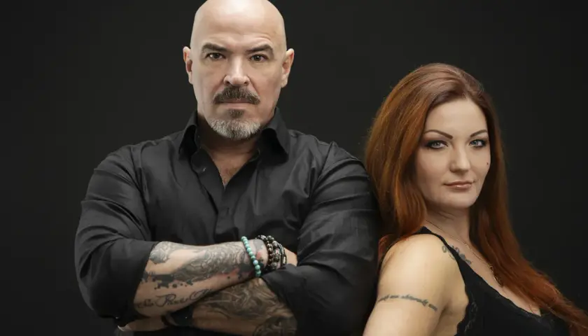 Caroline Grimwalker och en man med tatueringar och skägg står mot en svart bakgrund.