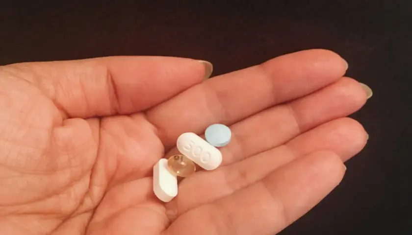 Dłoń trzyma kilka tabletek, w tym jedną z napisem "500". To może być wsparcie dla jelit, gdzie prebiotyk a probiotyk działają razem.