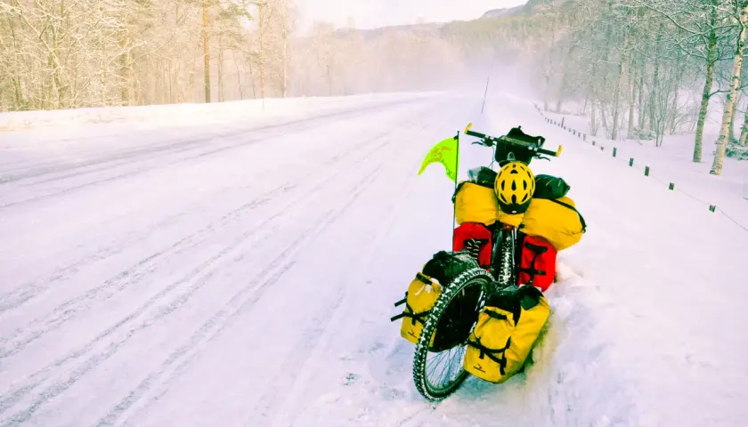 A fully loaded bicycle sits on a snowy road, a testament to adventure. The rider's concern about the brake fluid freezing point is evident in this winter scene.