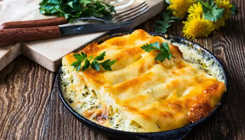 Zapiekane cannelloni w sosie, posypane serem i udekorowane natką pietruszki. Idealne danie na obiad.