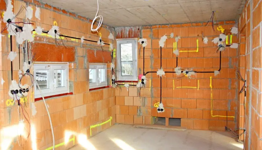 Schemat instalacji elektrycznej w nowym budynku. Widoczne przewody, puszki i oznaczenia na ścianach z cegły.
