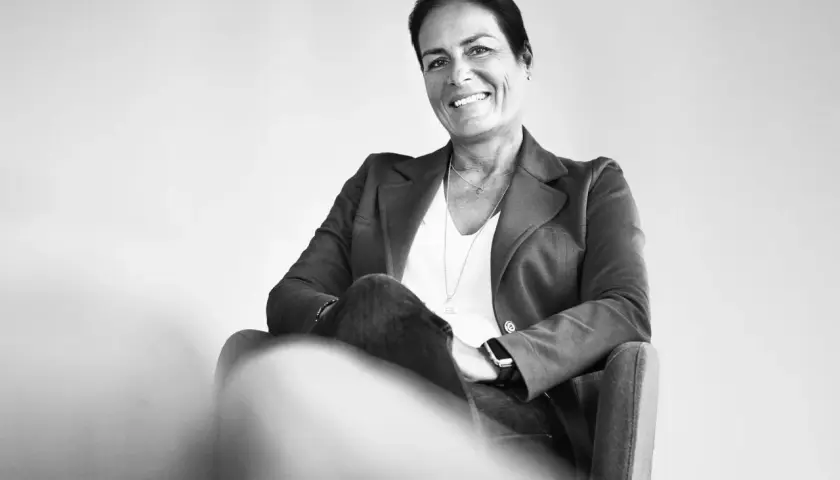 Manuela Reibold-Rolinger lächelt freundlich in die Kamera, während sie in einem Sessel sitzt. Sie trägt einen Blazer und Jeans.