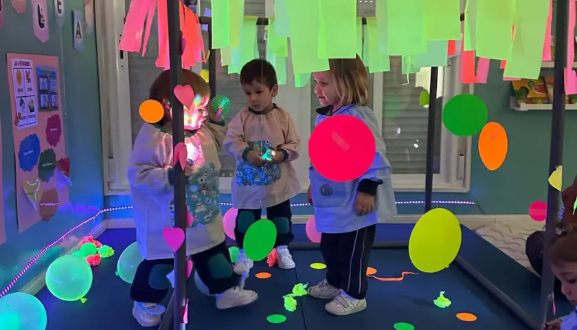Niños explorando un aula multisensorial infantil con luces de neón, globos y elementos interactivos.