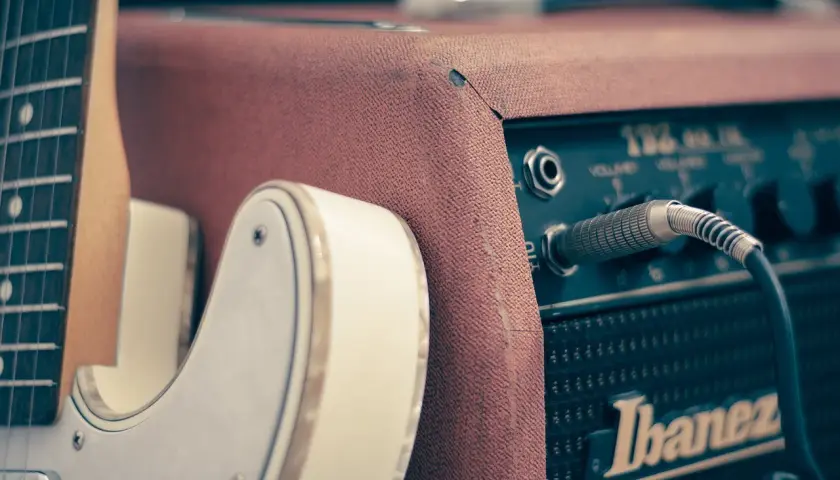 Biała gitara elektryczna podłączona do wzmacniacza Ibanez. Idealny zestaw, by dowiedzieć się, jak zacząć grać na gitarze elektrycznej.