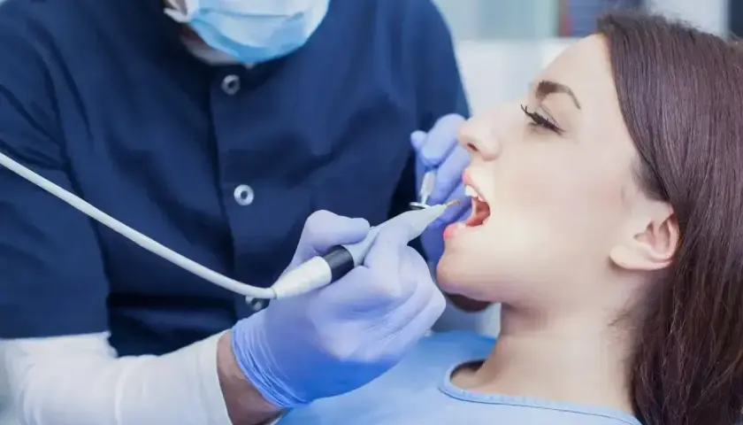 Dentysta w masce i rękawiczkach wykonuje zabieg. Zastanawiasz się, ile kosztuje znieczulenie u dentysty?