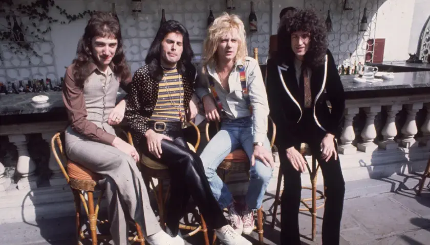 Freddie Mercury i zespół Queen siedzą przy barze w słoneczny dzień.