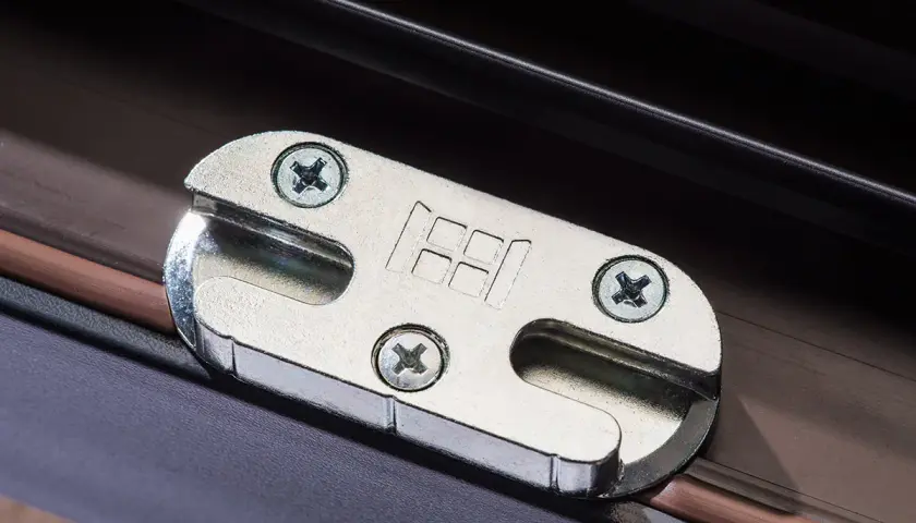Metalowe okucie okna z logo producenta, przykręcone do ramy okiennej.