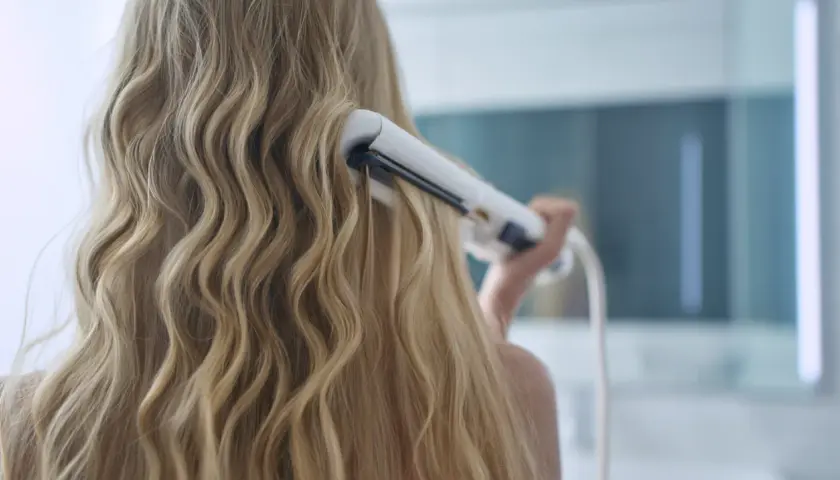 Kobieta kręci blond włosy lokówką, tworząc fale.