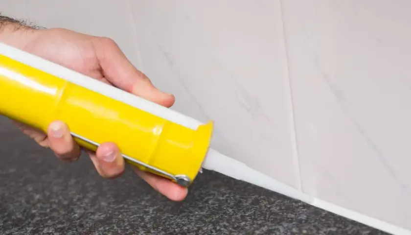 Mano aplicando silicona blanca con pistola en juntas de azulejo. Guía práctica de como aplicar silicona en juntas para un acabado perfecto.