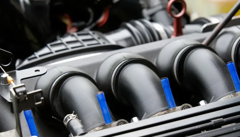 Detalle del colector de admisión de un coche, con tubos negros y pequeños detalles azules.