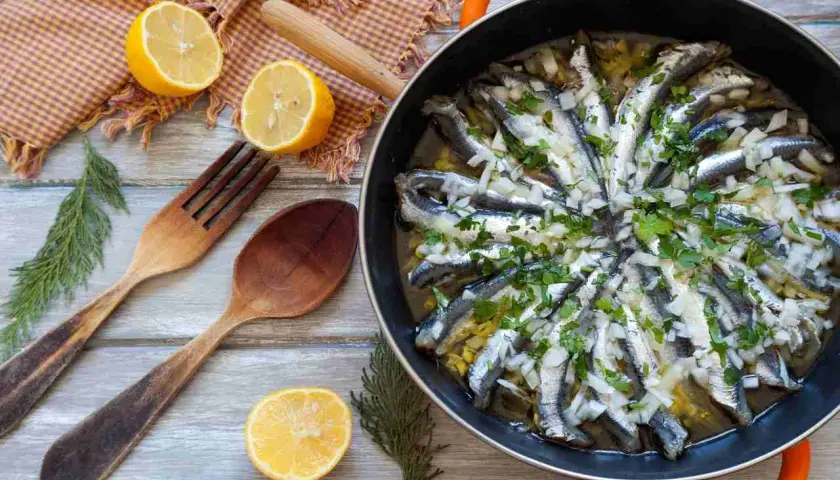Alici in padella, pronte per essere gustate, con limone, erbe aromatiche e cipolla. Un piatto semplice e saporito.