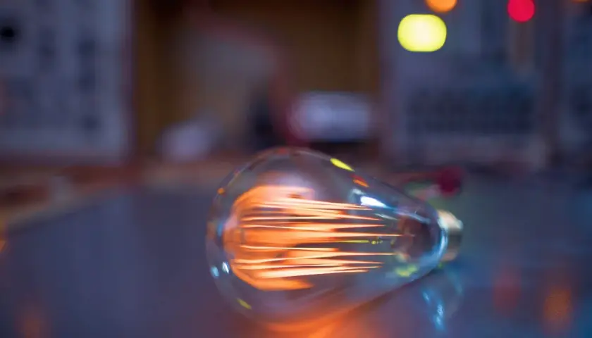 Żarówka LED 3W, ile to wat? Widoczna żarówka z rozżarzonym żarnikiem, w tle kolorowe światła.