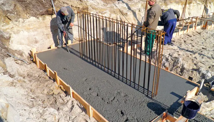 Budowa fundamentów: pracownicy wylewają beton na zbrojenie, tworząc solidny żelbeton.