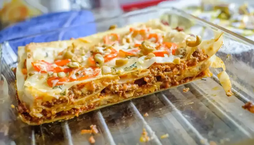 Pyszne, domowe piec lasagne z warstwami mięsa mielonego, makaronu i sera, ozdobione pomidorami i oliwkami.