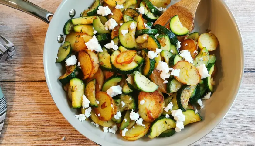 Herzhafte zucchini pfanne mit goldbraunen Kartoffelscheiben und zerbröseltem Feta, garniert mit frischen Kräutern.