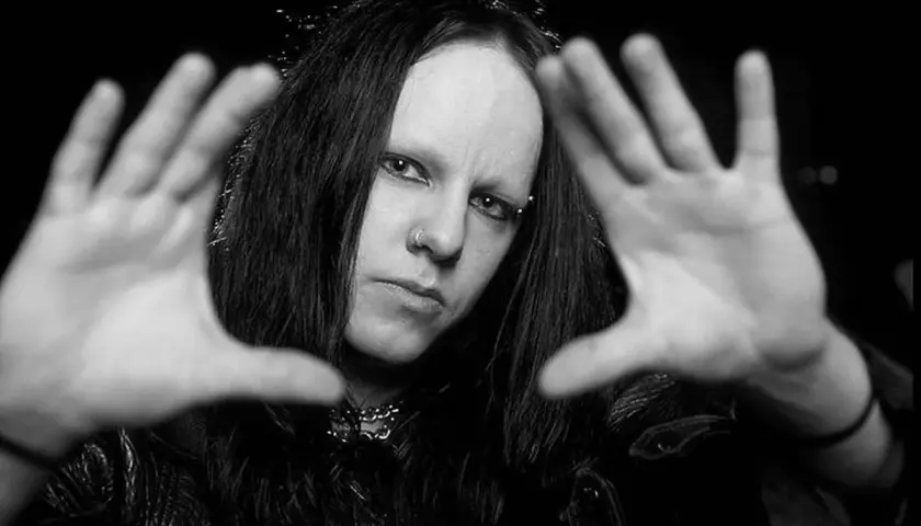 Joey Jordison, perkusista zespołu Slipknot, z rękami przed twarzą, w czerni i bieli.