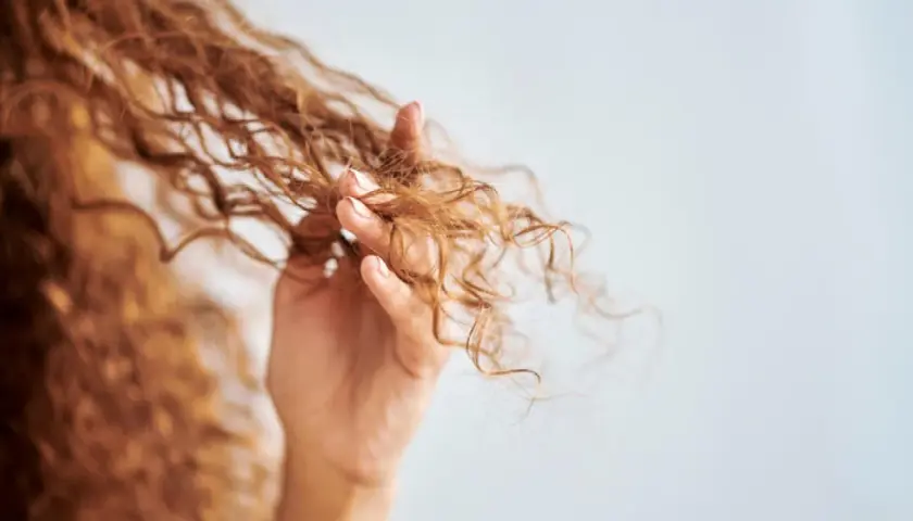 Mano acariciando cabello rizado, mostrando cómo rizar el pelo con espuma para definir ondas.