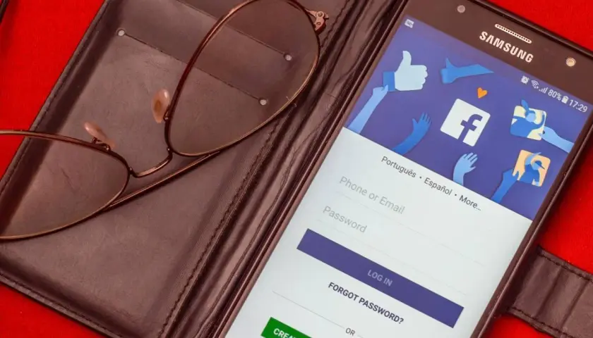 Okulary leżą na etui z telefonem wyświetlającym ekran logowania Facebooka.