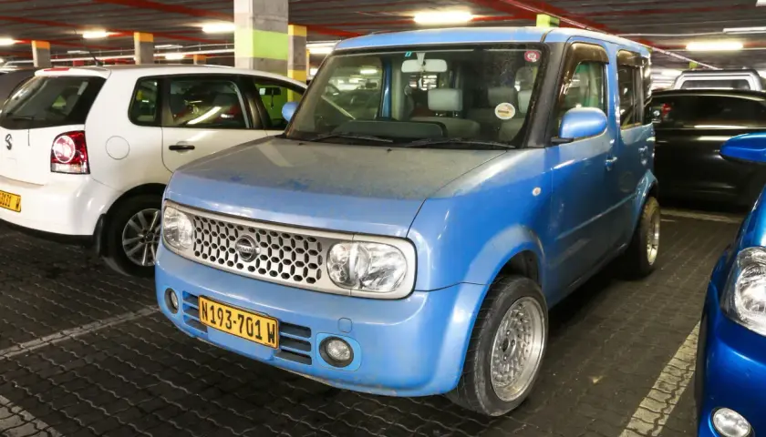 Niebieski Nissan Cube z tablicą rejestracyjną N193-701 W zaparkowany obok białego Volkswagena.