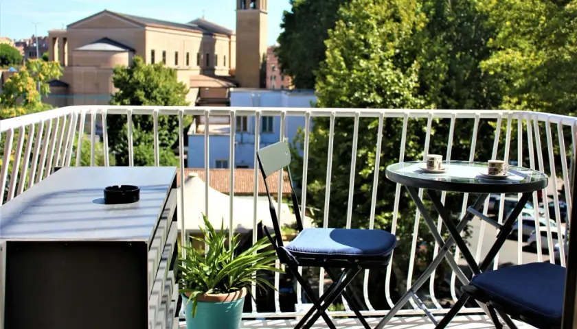 Idealne miejsce, gdzie nocować w Rzymie: balkon z widokiem na kościół i drzewa, stolik z kawą czeka.
