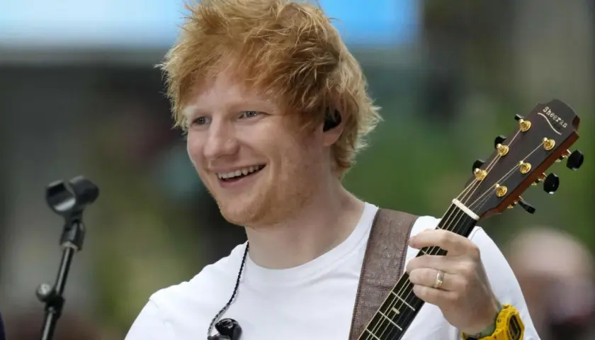 Ed Sheeran uśmiecha się, grając na gitarze podczas koncertu w Polsce.