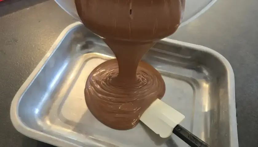 Une ganache au chocolat, inspirée par le Toblerone, est versée dans un plat métallique. Une spatule aide à l'étaler.