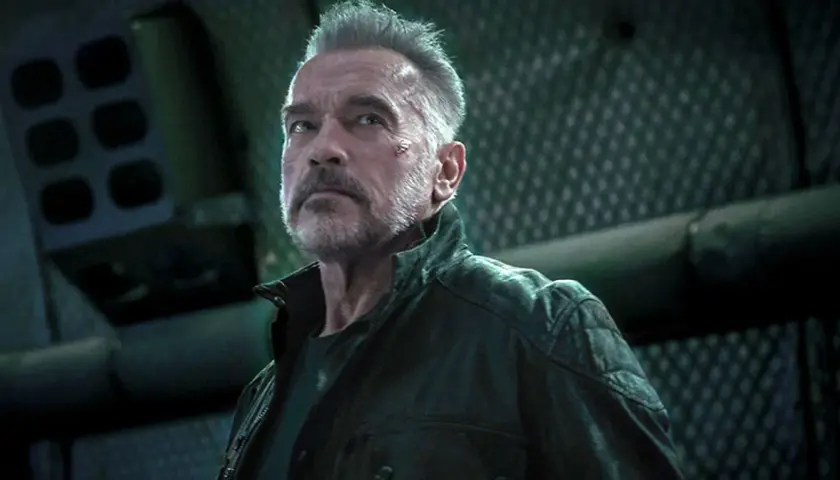 Arnold Schwarzenegger jako T-800 w filmach Jamesa Camerona. Z blizną na policzku, w skórzanej kurtce, patrzy w górę.