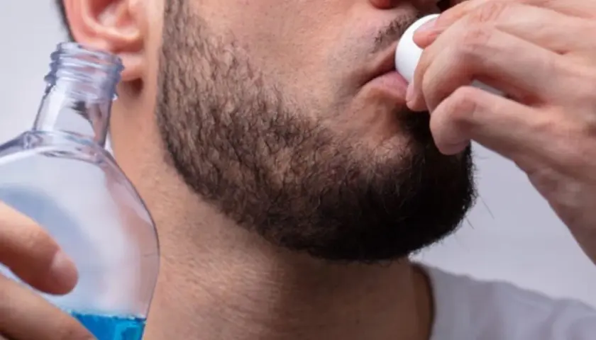 Uomo usa collutorio per parodontite, tenendo una bottiglia di liquido blu.