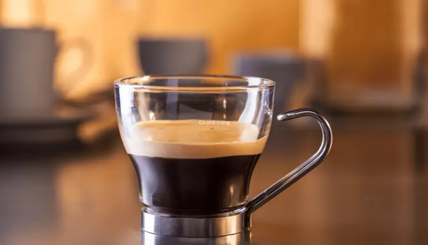 Kawa ristretto w szklanej filiżance z metalowym uchem. Kremowa pianka na ciemnym espresso.