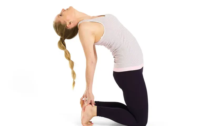Kvinna i kamelen yoga-ställning, med ryggen böjd bakåt och händerna vid fötterna. Håret är flätat.
