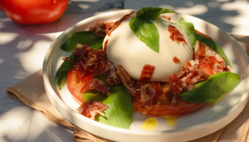 Deliciosa ensalada de burrata con tomates, albahaca fresca y crujiente jamón serrano.