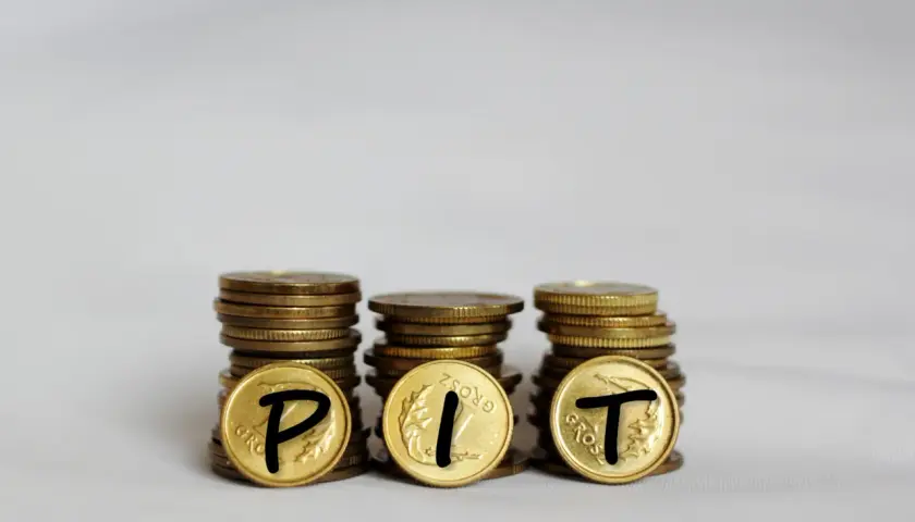 Trzy stosy monet, na których widnieją litery P, I, T. Symbolizują one rozliczenie podatku PIT.