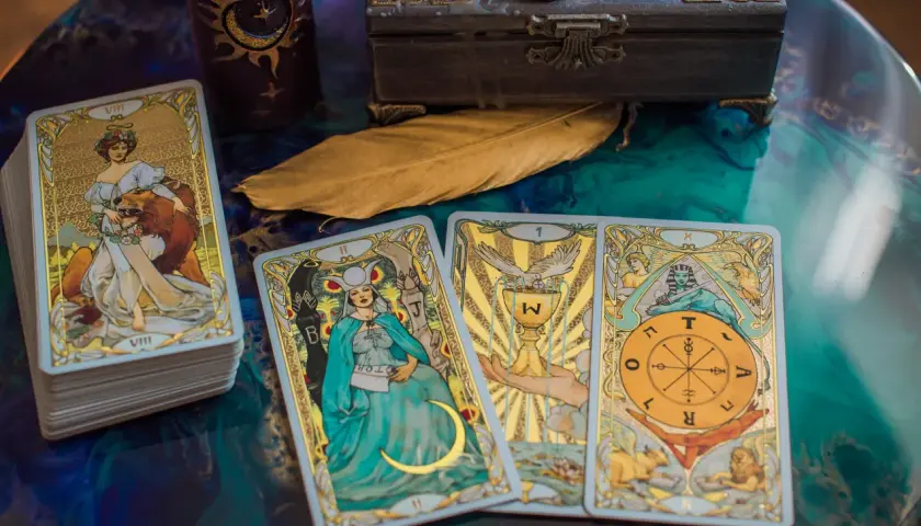 Tarot byk miesięczny: talia kart z wizerunkami postaci i symboli, w tym karta z bykiem, świeca, skrzynia i pióro.
