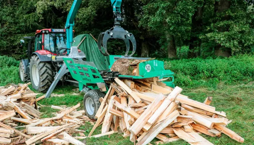 Ein Traktor mit einem Holzspalter, der gerade einen Baumstamm zerteilt. Ein gebrauchter Schichtholzspalter im Einsatz.