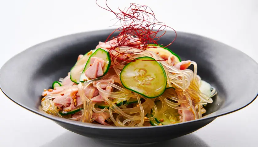 A refreshing harusame salad with glass noodles, sliced cucumber, and ham, garnished with delicate red chili threads.