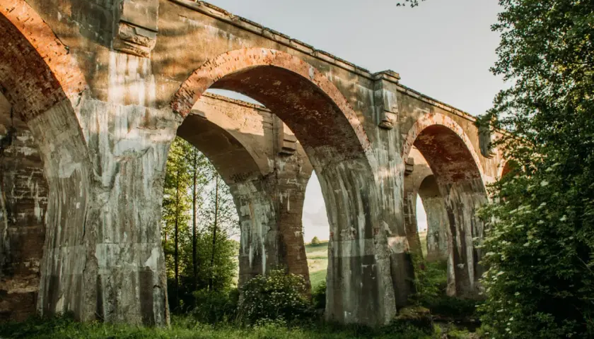 Imponujące, stare mosty w Kiepojciach, porośnięte zielenią, stoją dumnie pod błękitnym niebem.