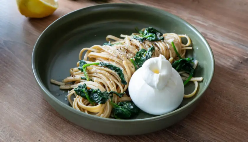 Zitronen Pasta mit Spinat und Burrata auf einem grünen Teller, daneben eine Zitronenhälfte.