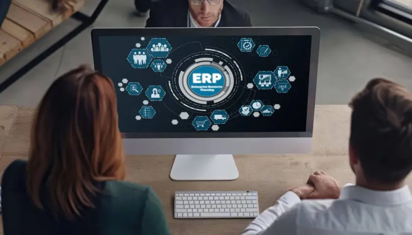 Zespół analizuje diagram ERP na ekranie komputera. Ikony symbolizują różne moduły systemu, od zarządzania zasobami ludzkimi po logistykę.