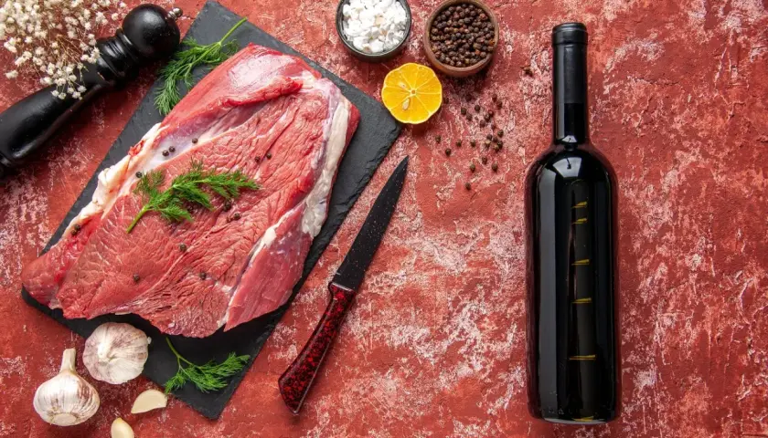 Un morceau de viande crue, prêt pour un repas savoureux avec un vin rouge. Des épices, de l'ail et une tranche de citron complètent la scène.