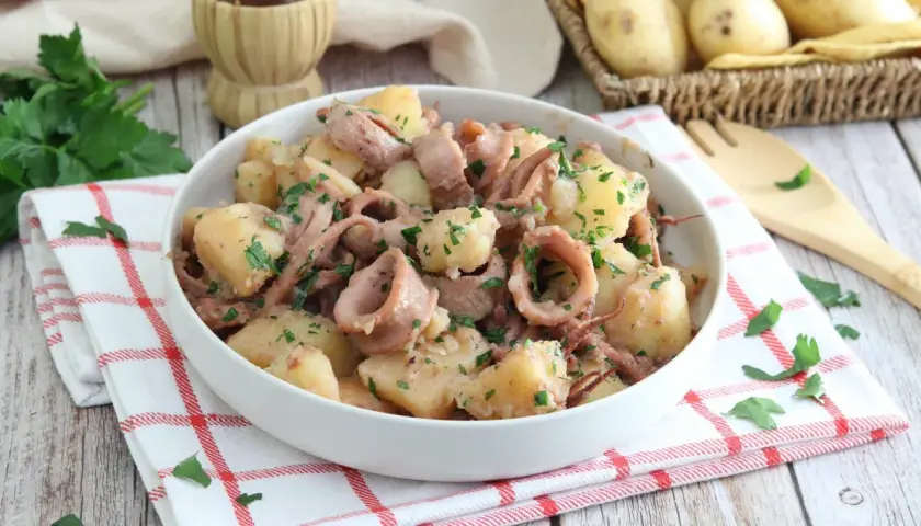 Un saporito piatto di totani e patate, condito con prezzemolo fresco, servito in una ciotola bianca su un tovagliolo a quadri rossi.