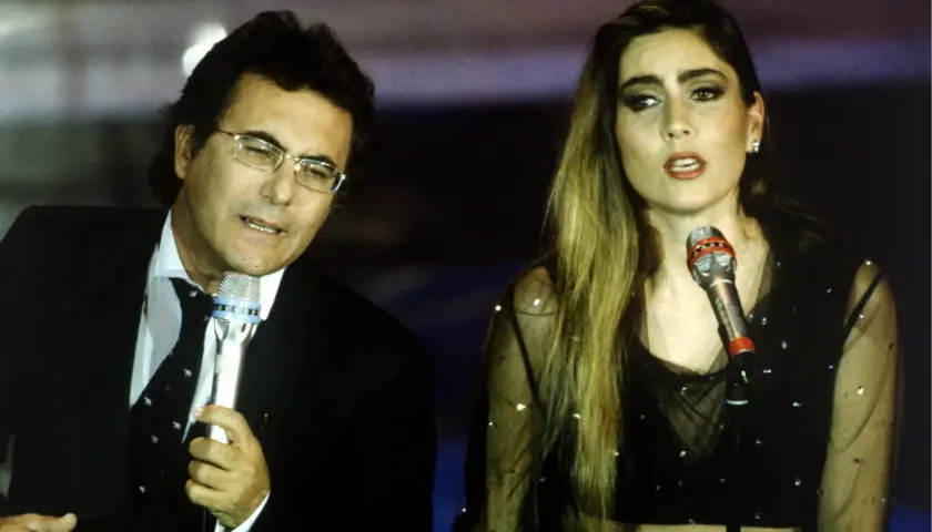 Al Bano i jego nowa partnerka na scenie, w blasku świateł, śpiewają do mikrofonów.