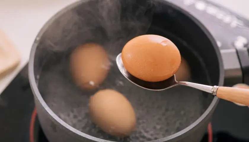 Une cuillère sort un œuf à la coque de l'eau bouillante. Trois autres œufs sont dans la casserole.